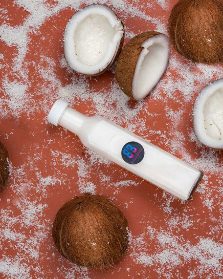White coconut cocktail in a bottle next to coconuts sprinkles and fruits in the background