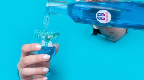 Two hands ripping through blue background pouring blue candy cocktail inside a shot glass