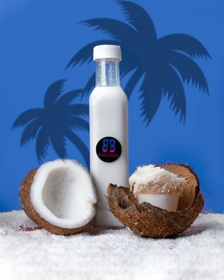 White cocktail in a bottle next an open coconut in a blue tropical background