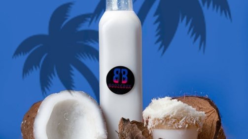 White cocktail in a bottle next an open coconut in a blue tropical background