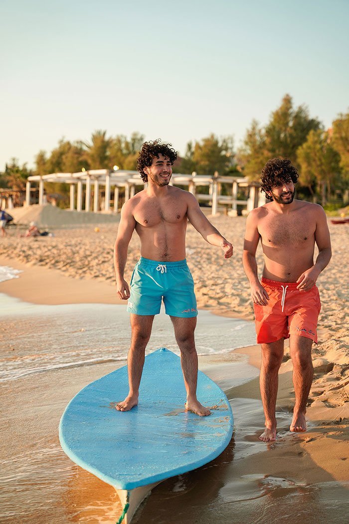Two Young Men Models in the beach Wearing Blue and Orange Swimwear