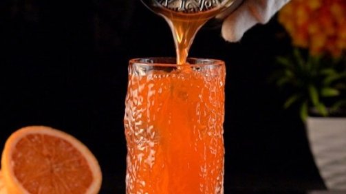 Orange cocktail being poured from skull Hawthorne strainer into possessed ancient glass