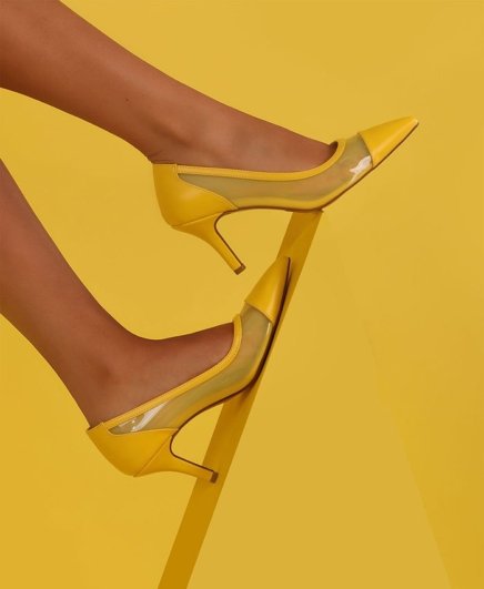 Yellow pair of fashion heels worn by a woman model displayed on a yellow background