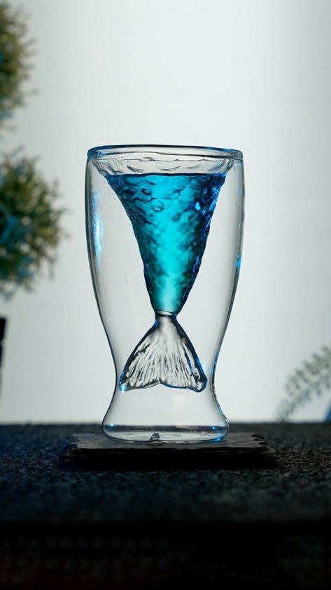 Blue Cocktail in mermaid's tail glass around a white background