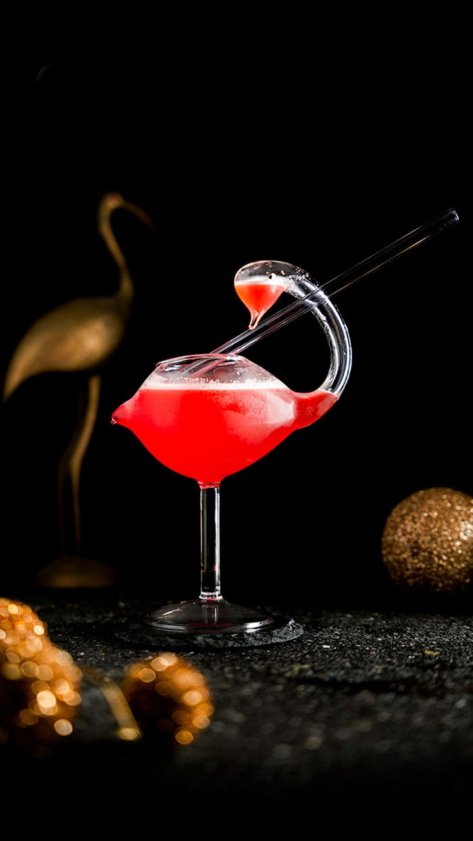 Red Cocktail inside Flamingo Cocktail Glass around gold props in the background