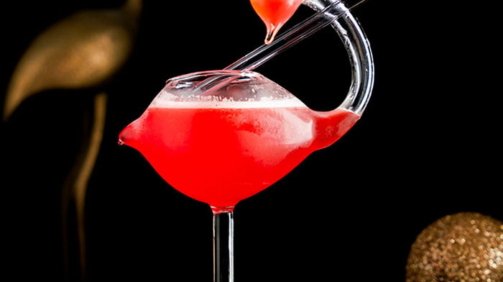 Red Cocktail inside Flamingo Cocktail Glass around gold props in the background