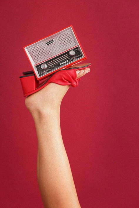 one foot of a woman model wearing red heels pushing on an old stereo around a red background