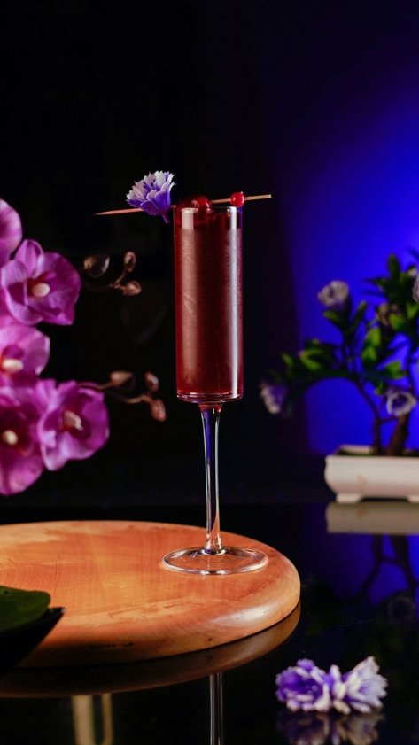 Red cocktail in champagne glass around colorful flowerful background