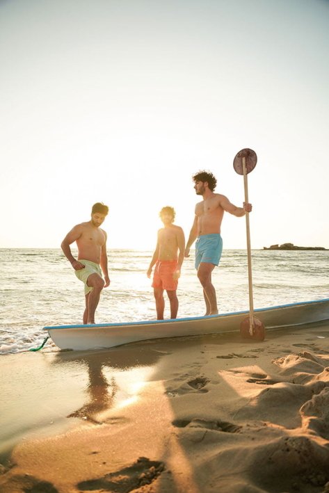 Three young men models in the beach wearing blue and green and orange swimwear