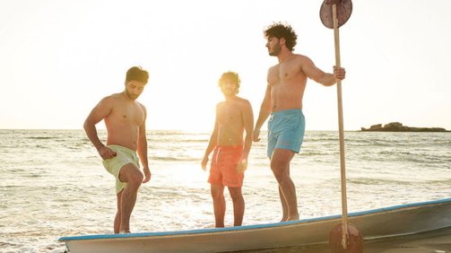 Three young men models in the beach wearing blue and green and orange swimwear