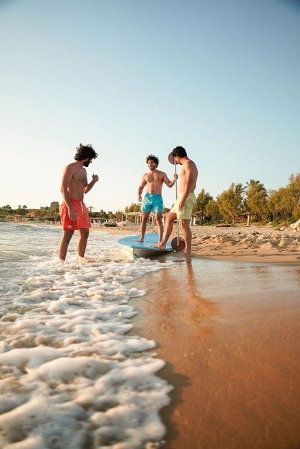 Three young men models in the beach wearing blue and green and orange swimwear