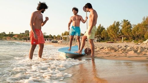Three young men models in the beach wearing blue and green and orange swimwear