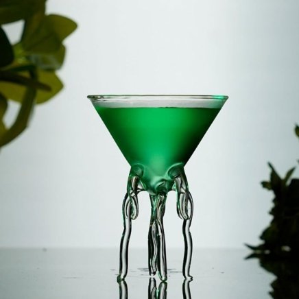 Green cocktail vodka stinger in a tiny octopus martini glass around a white background
