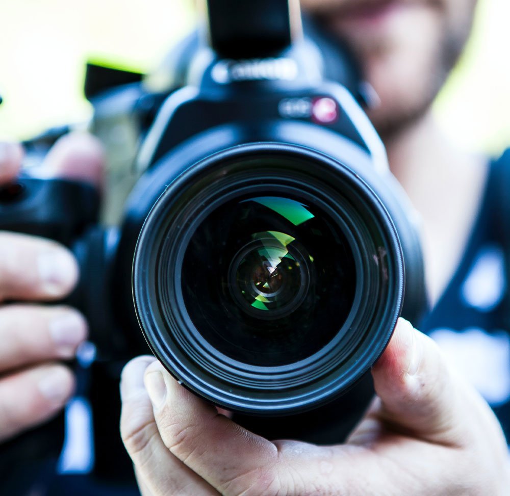videographer carrying a camera with the lens pointing at the viewer.